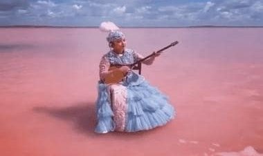 With pink-coloured lake in backdrop, Kazakh woman plays dombyra at Lake Kobeytuz